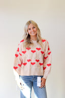 Woman wearing a cream sweater with red heart patterns against a plain background